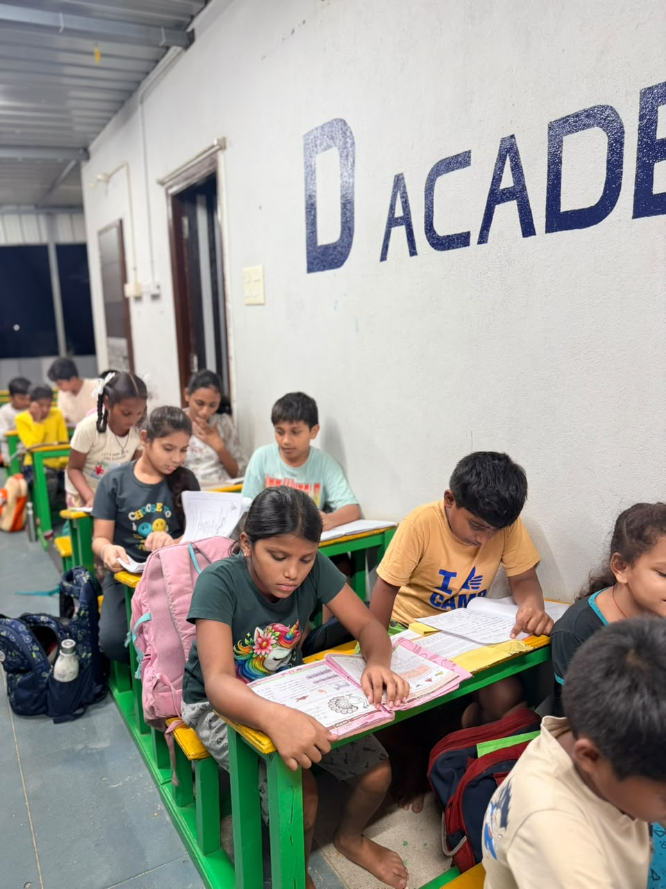 D Academy students reading their books at green desks beside the D Academy wall sign