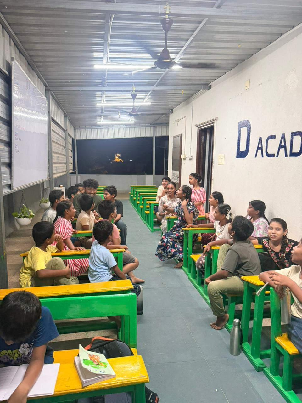 An evening class at D Academy with students seated at green and yellow desks